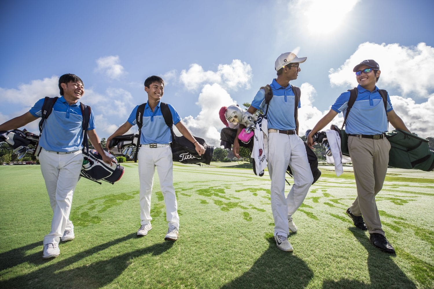 Four IJGA student-athletes in blue polos walk together on the golf course holding their bags