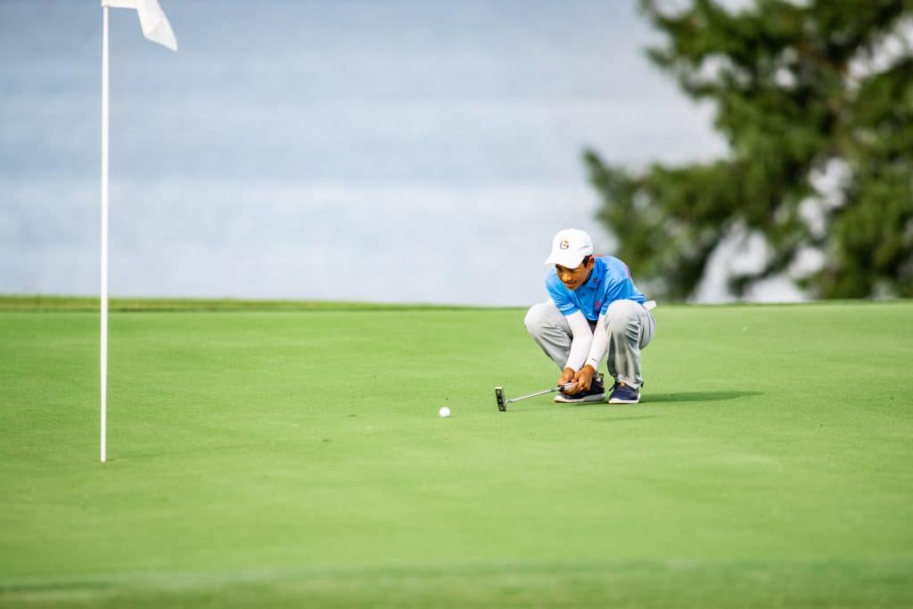 Golfer leans down on the greens watching the golf ball