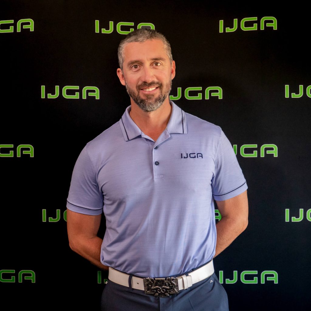 IJGA coach Andres Rodriguez, smiles against a black IJGA logo background