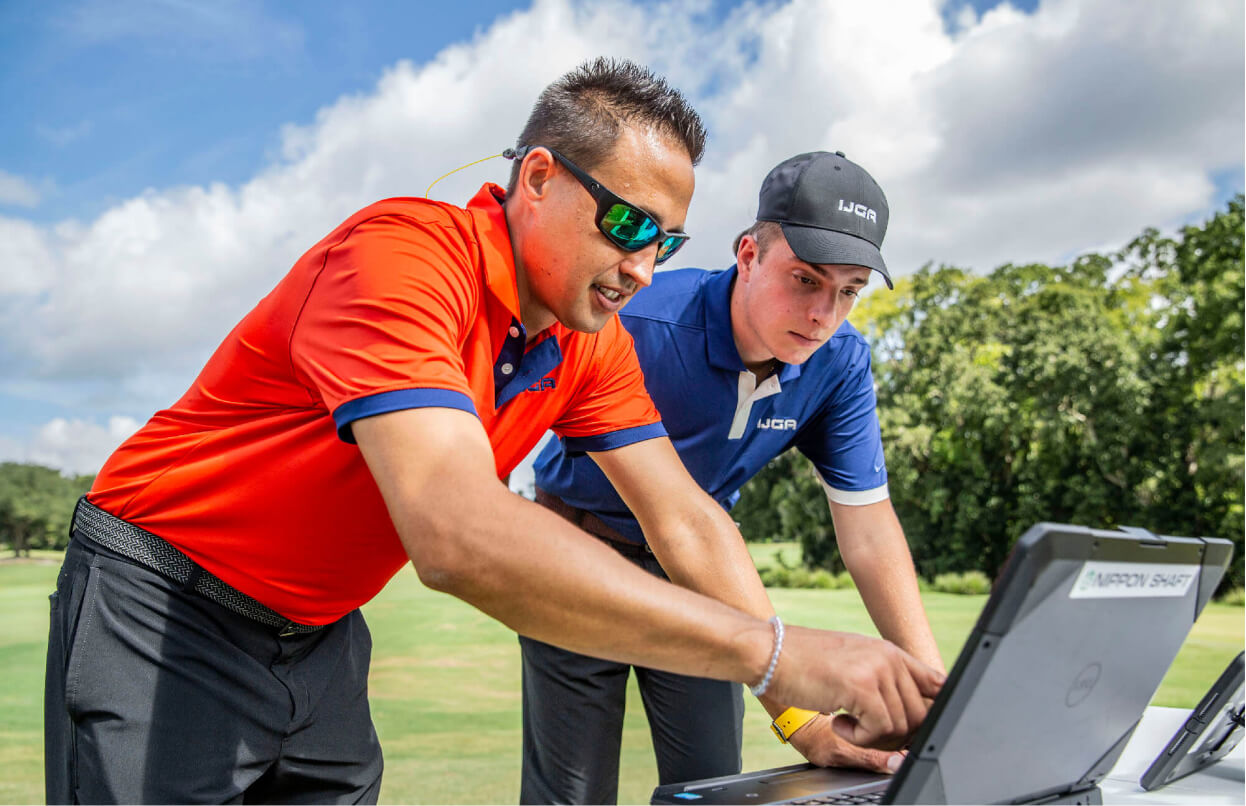 A coach and IJGA golfer stand together on the course, looking at a laptop