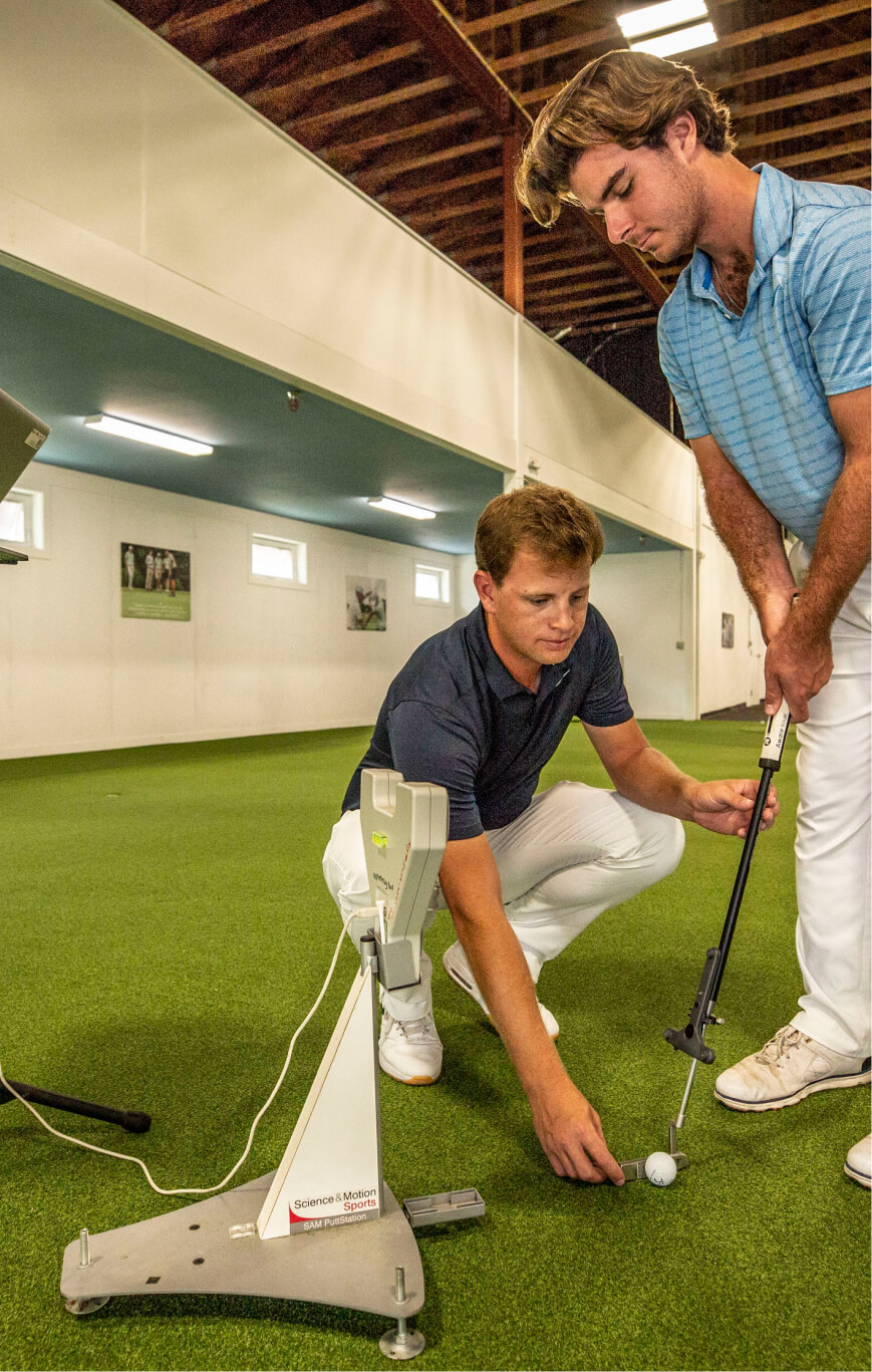 A coach squats down to help a golfer putt