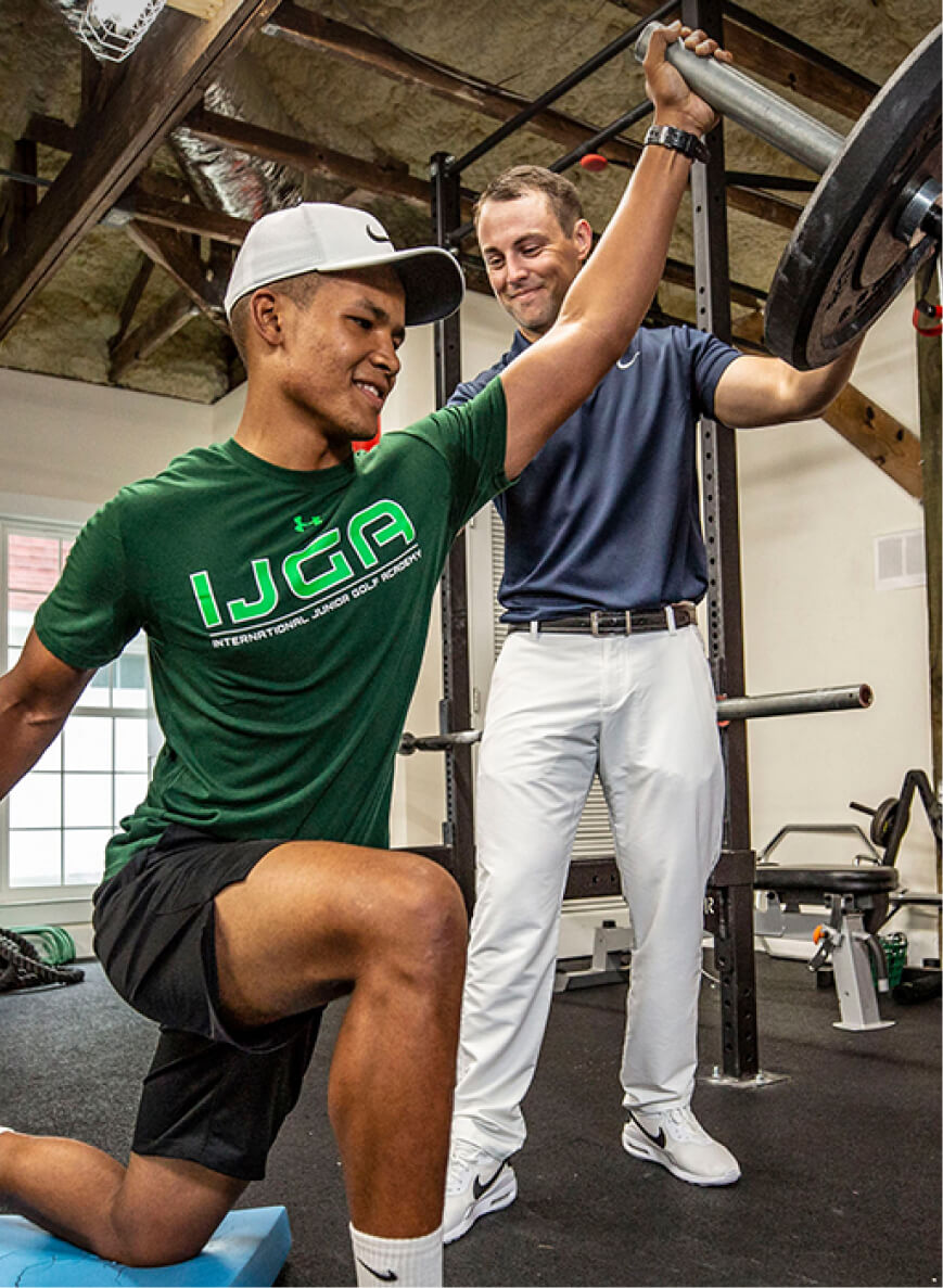 a coach assists IJGA student-athlete lifting weights