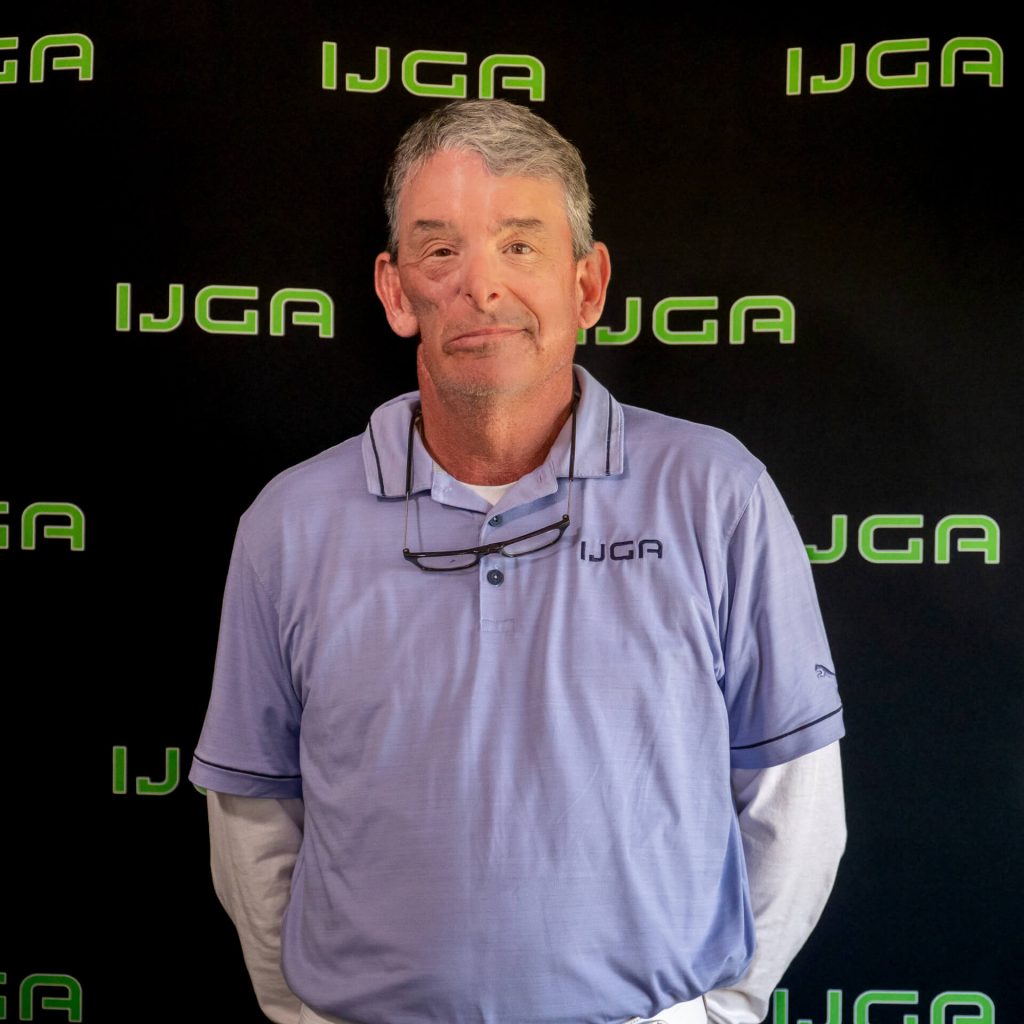 IJGA coach Hugh Royer, smiles against a black IJGA logo background