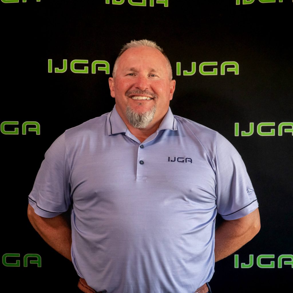 IJGA coach John Gaylen, smiles against a black IJGA logo background