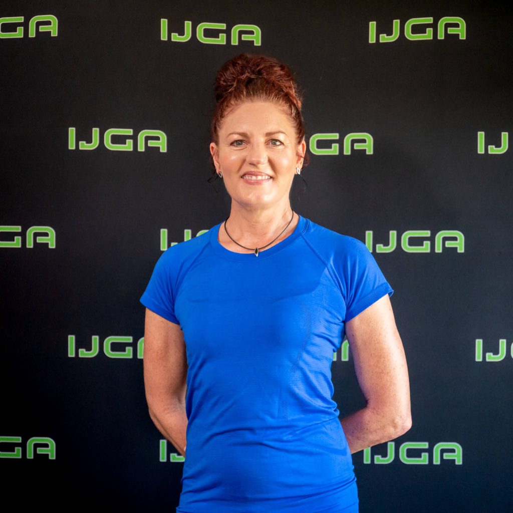 IJGA coach Karen Harrison, smiles against a black IJGA logo background