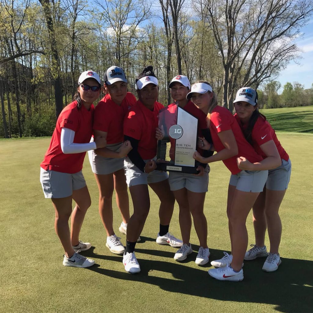 Women's college golf team holds up a Big Ten trophy on the golf course