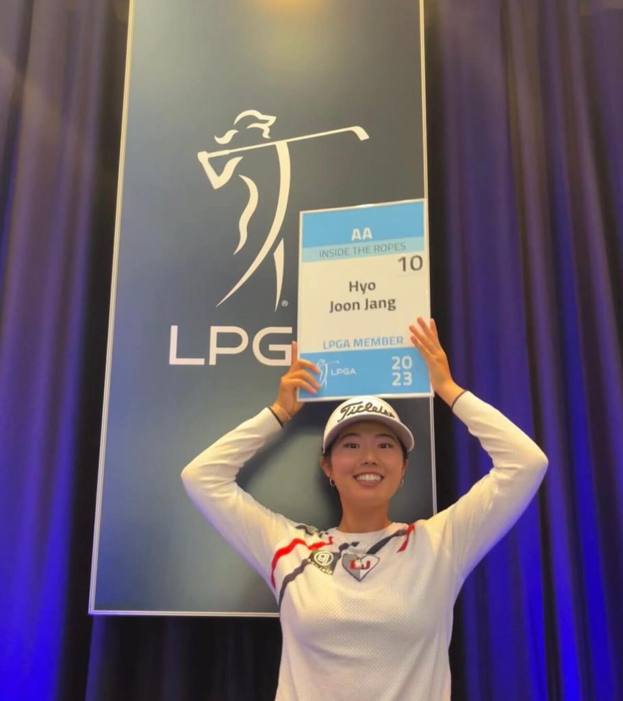 Hyo Joon Jang, a female golfer, holds a sign above her head that states her name and the fact that she has earned her LGPA tour card.