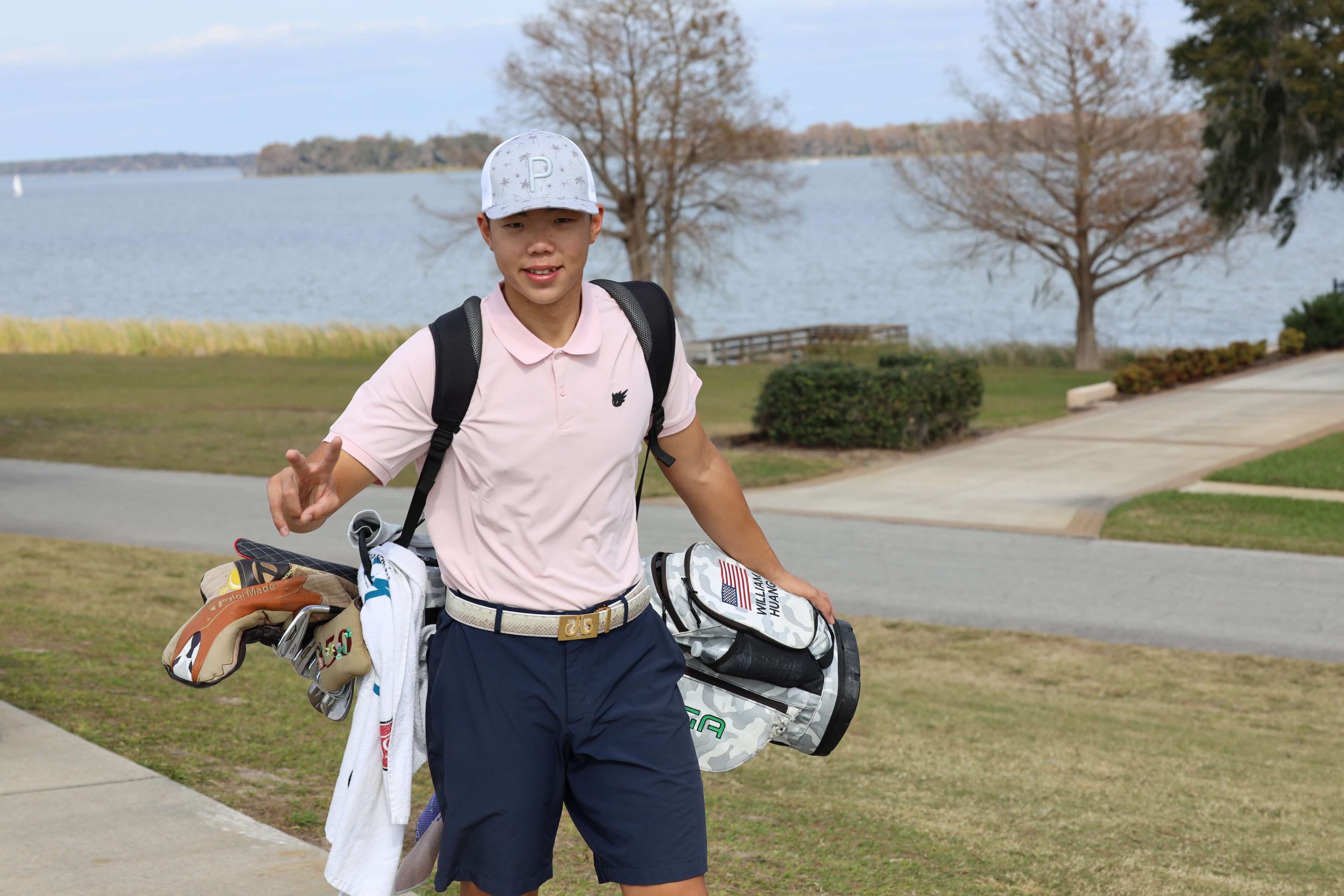 A golfer holding an IJGA bag walks on the course and gives a peace sign to the camera
