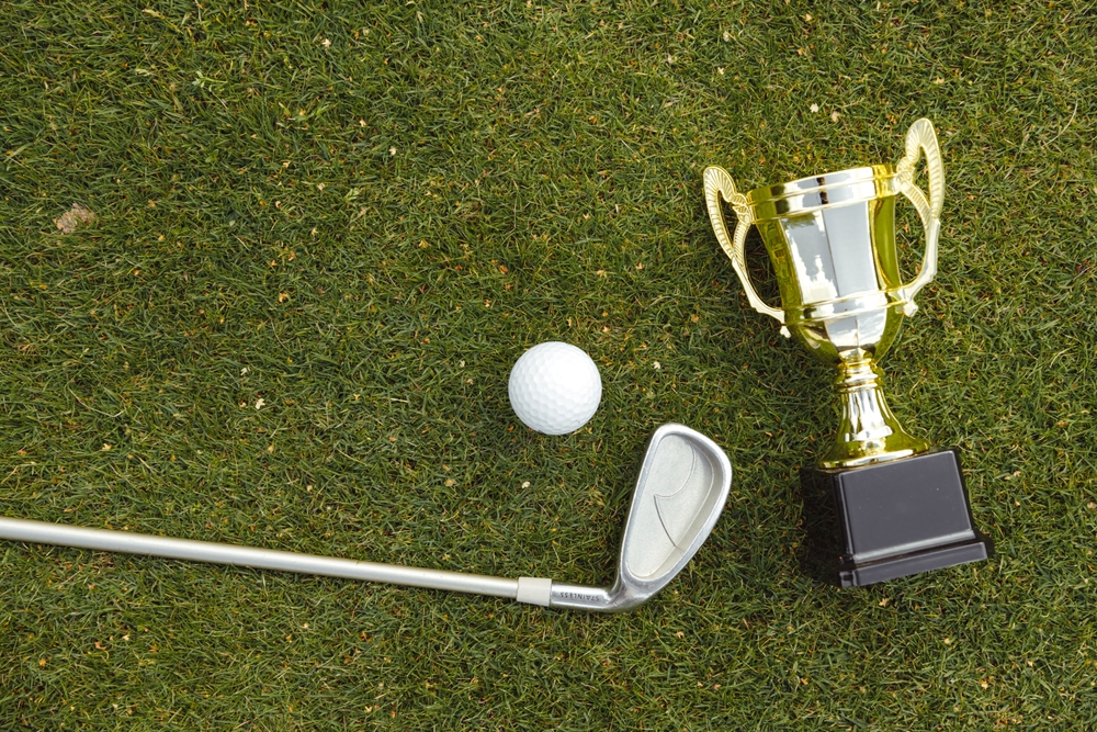 A club, golf ball, and trophy lie on the grass on a golf course