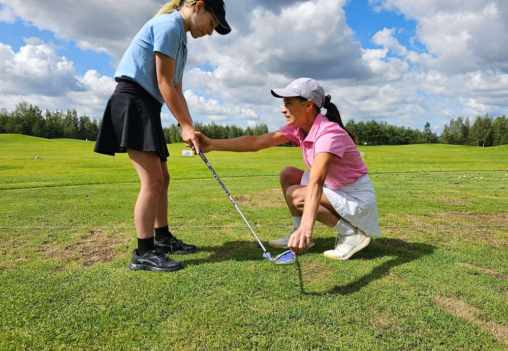 Coach demonstrates proper golf techniques to a junior golf student