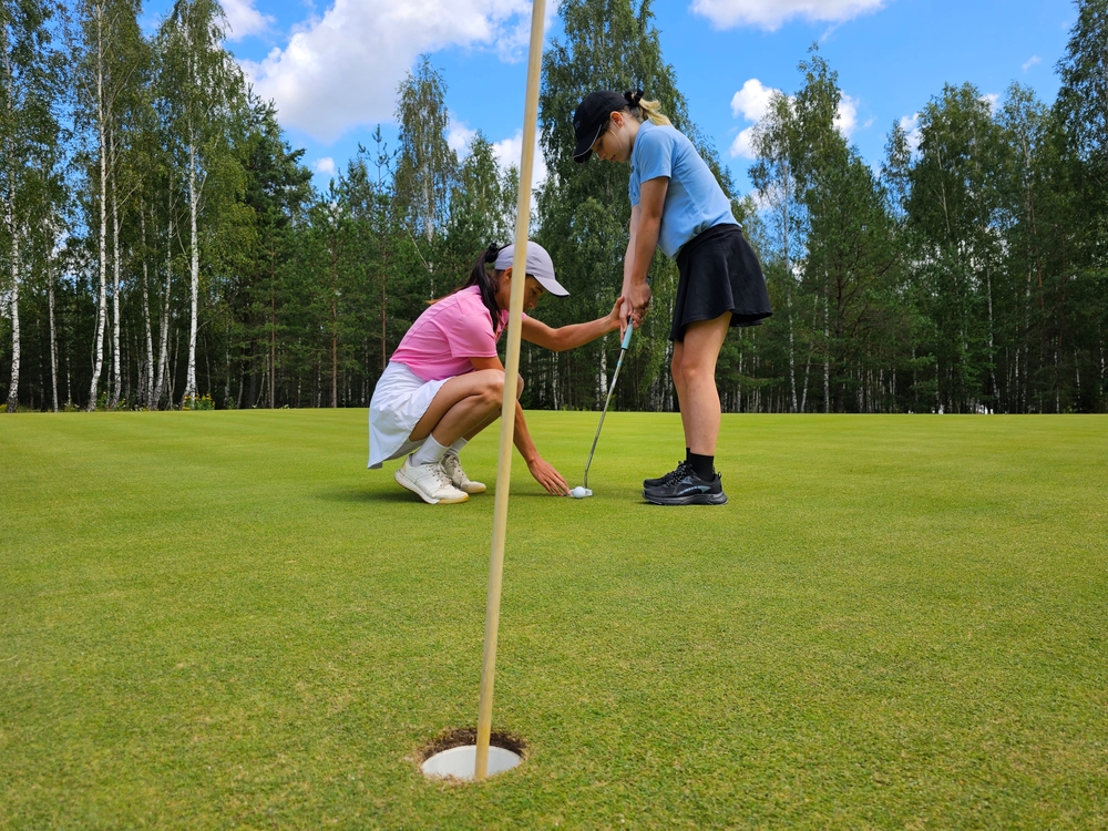 A junior golfer and coach practicing on the green