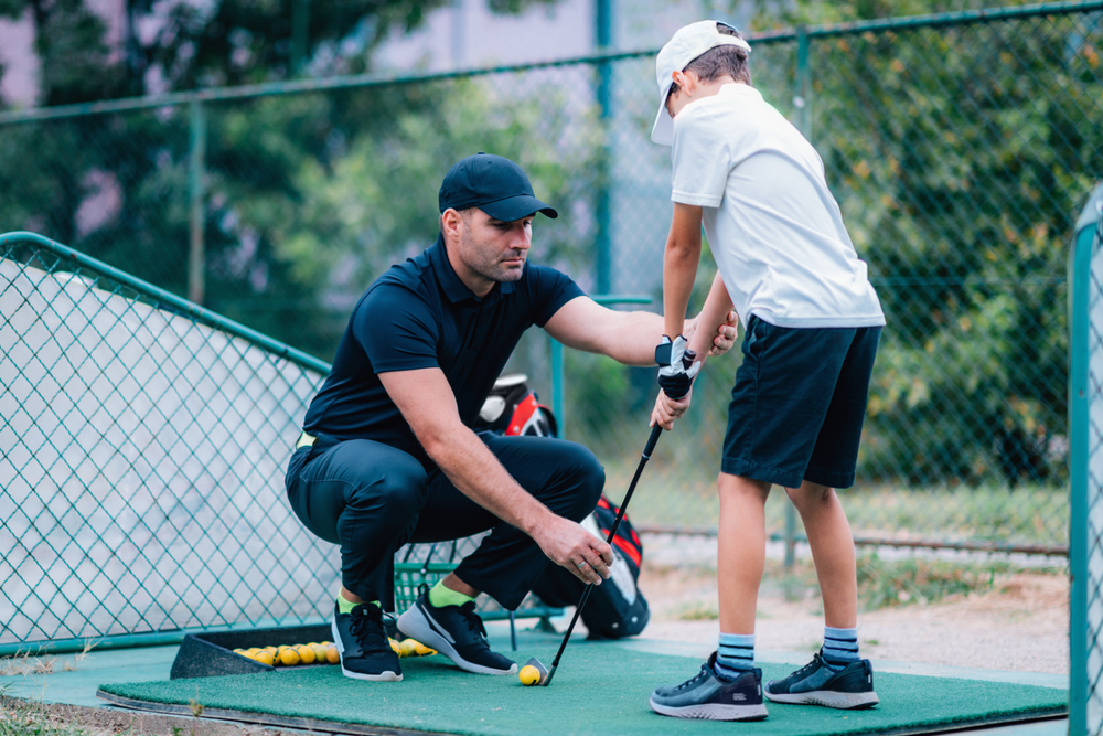 A junior golfer practicing with his coach