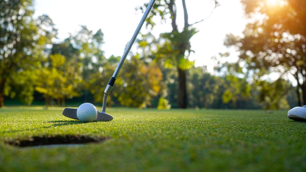 Close-up of a golf club, golf ball, and tee on a green